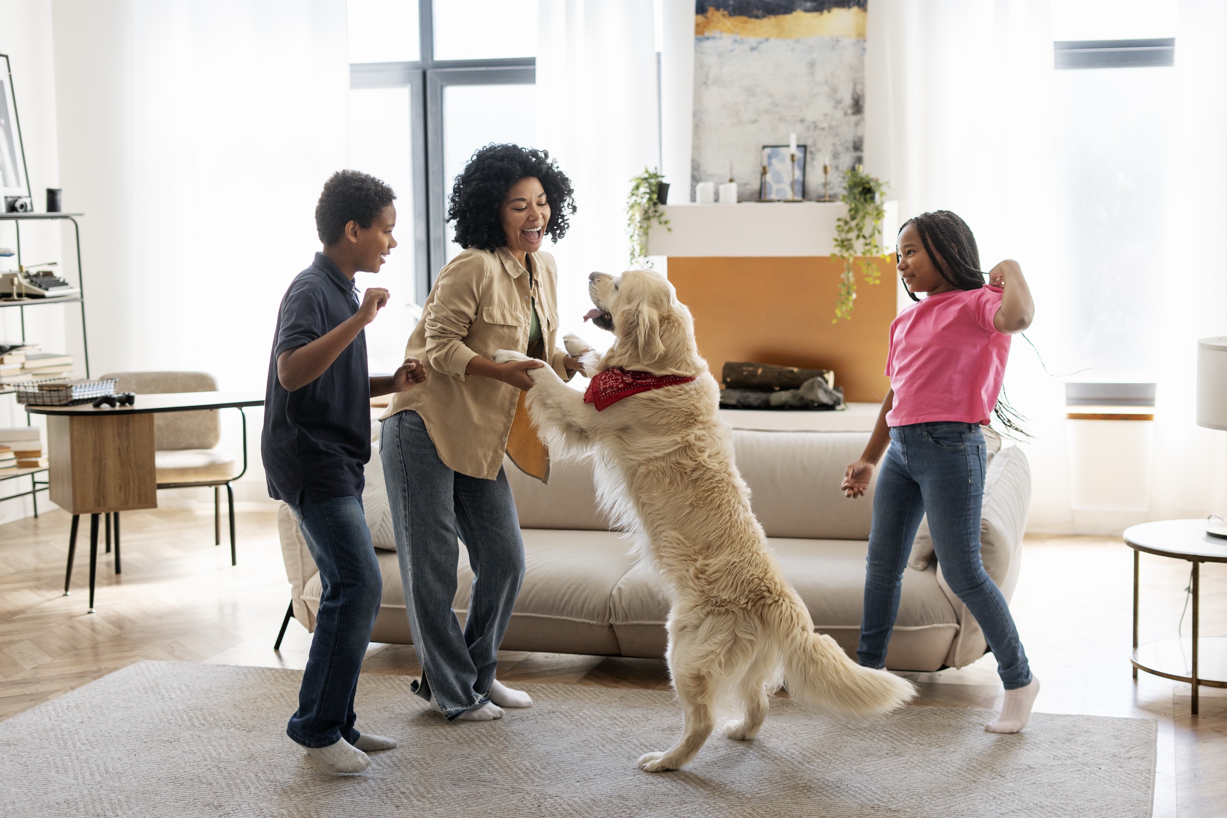 A mother and two children playing with their golden retriever in the living room
